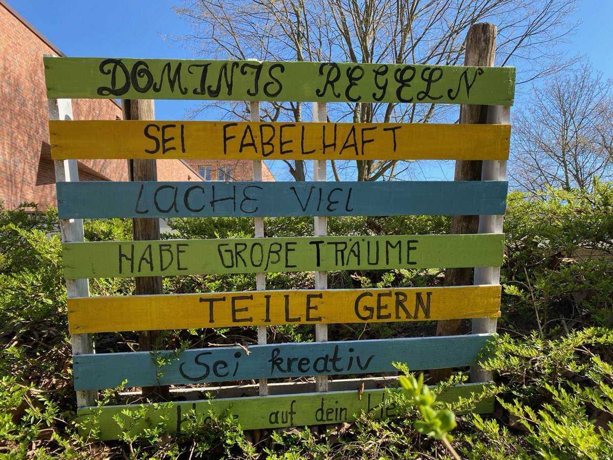 Bunt bemalte Holzpalette mit den Dominis-Regeln, u. a. „Sei fabelhaft“, „Lache viel“, „Habe große Träume“
